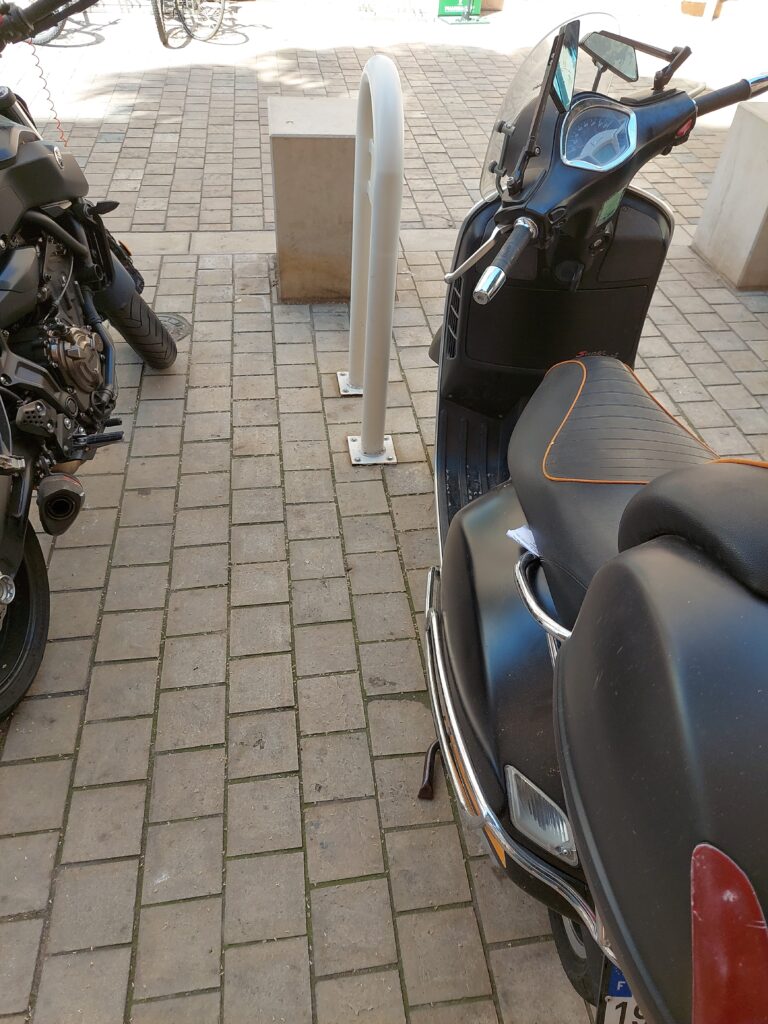 Un scooter garé à côté d'un arceau, avec une notice de verbalisation attachée. :)
