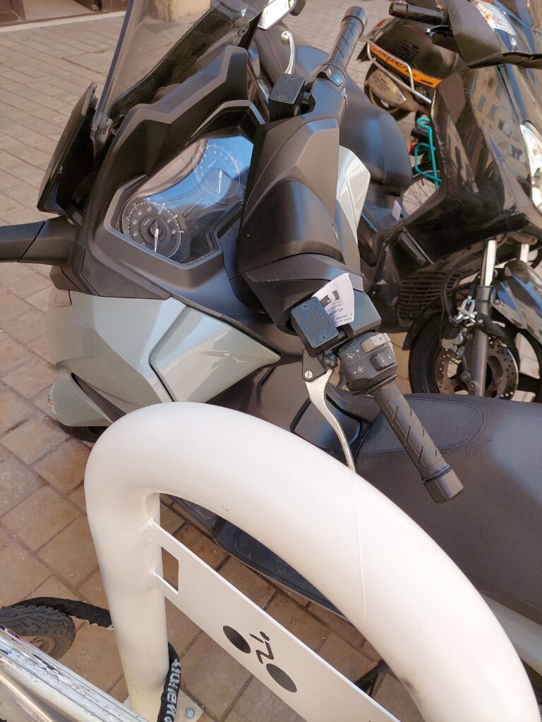 Un scooter garé à côté d'un arceau, avec une notice de verbalisation attachée. :)