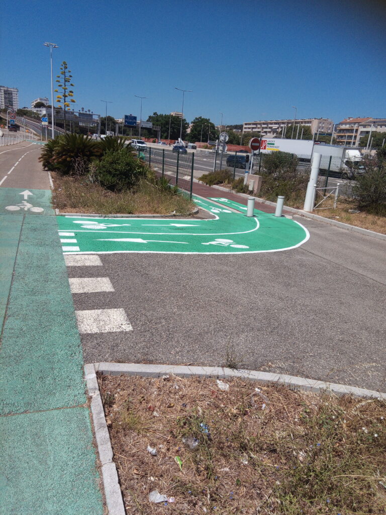 Photo du embranchement entre la piste du littoral et la passerelle sur l'autoroute, niveau palais du sport. Le cheminement pour les cyclistes est désormais bien visible et compréhensible dans les deux sens.